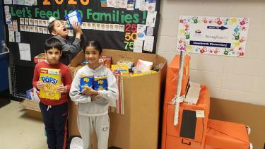 Three students stand in front of large box filled with food donations