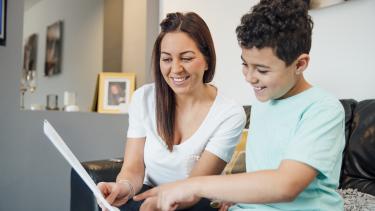 A boy and his mother are looking at the child's report card together at home.