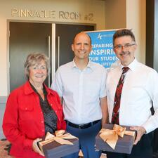 Male principal stand between one female retiree and one male retiree, they are smiling for the photo